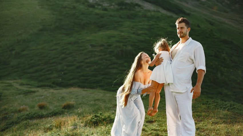 A joyful family of three in white clothing enjoying the outdoors on a sunny day.